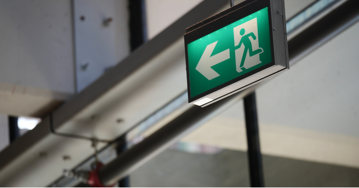 Backlit emergency exit sign with white arrow and figure, framed in a metal light box.